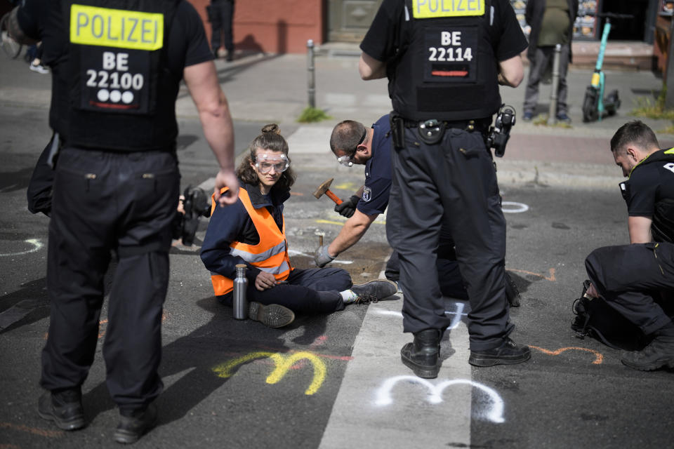 A police officer uses a hammer and chisel to remove a climate activist who has glued himself to a road during a climate protest in Berlin, Germany, Monday, May 22, 2023. (AP Photo/Markus Schreiber)