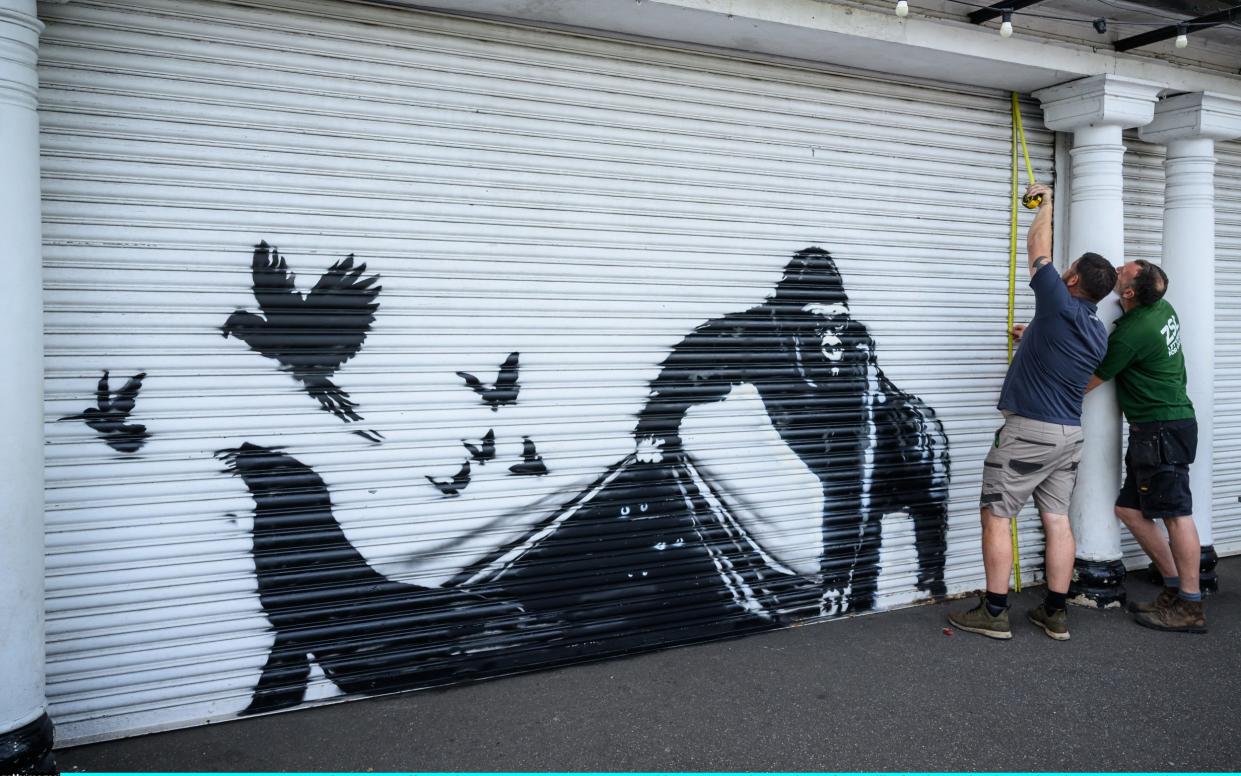 London Zoo staff members measure up a new mural by street artist Banksy of a gorilla freeing animals on the shutters at London Zoo