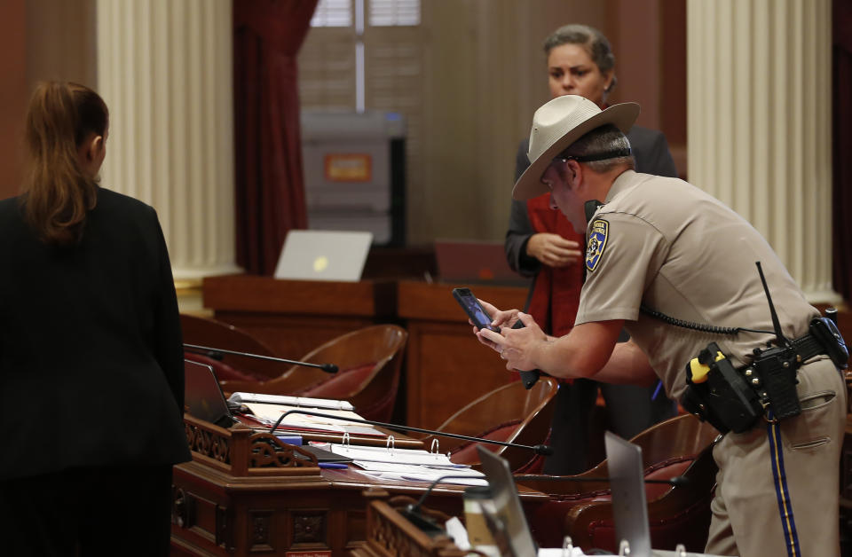 A California Highway Patrol Officer photographs a desk on the Senate floor after a red liquid was thrown from the Senate Gallery during the Senate session at the Capitol in Sacramento, Calif., Friday, Sept. 13, 2019. The Senate was cleared as an investigation is taking place. Authorities took a person into custody.(AP Photo/Rich Pedroncelli)