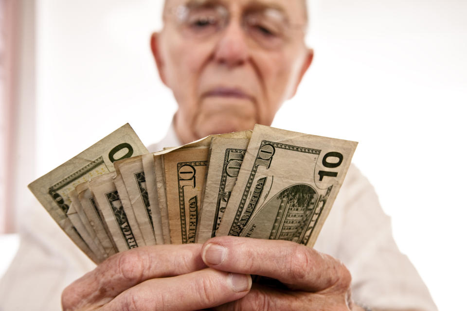 An elderly man counting a fanned pile of cash bills in his hands.