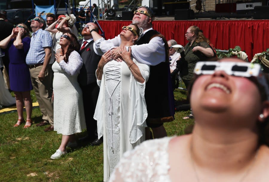 RUSSELLVILLE, ARKANSAS – APRIL 08: Couples view the solar eclipse during a mass wedding at the Total Eclipse of the Heart festival on April 8, 2024 in Russellville, Arkansas. Millions of people have flocked to areas across North America that are in the “path of totality” in order to experience a total solar eclipse. During the event, the moon will pass in between the sun and the Earth, appearing to block the sun. (Photo by Mario Tama/Getty Images)