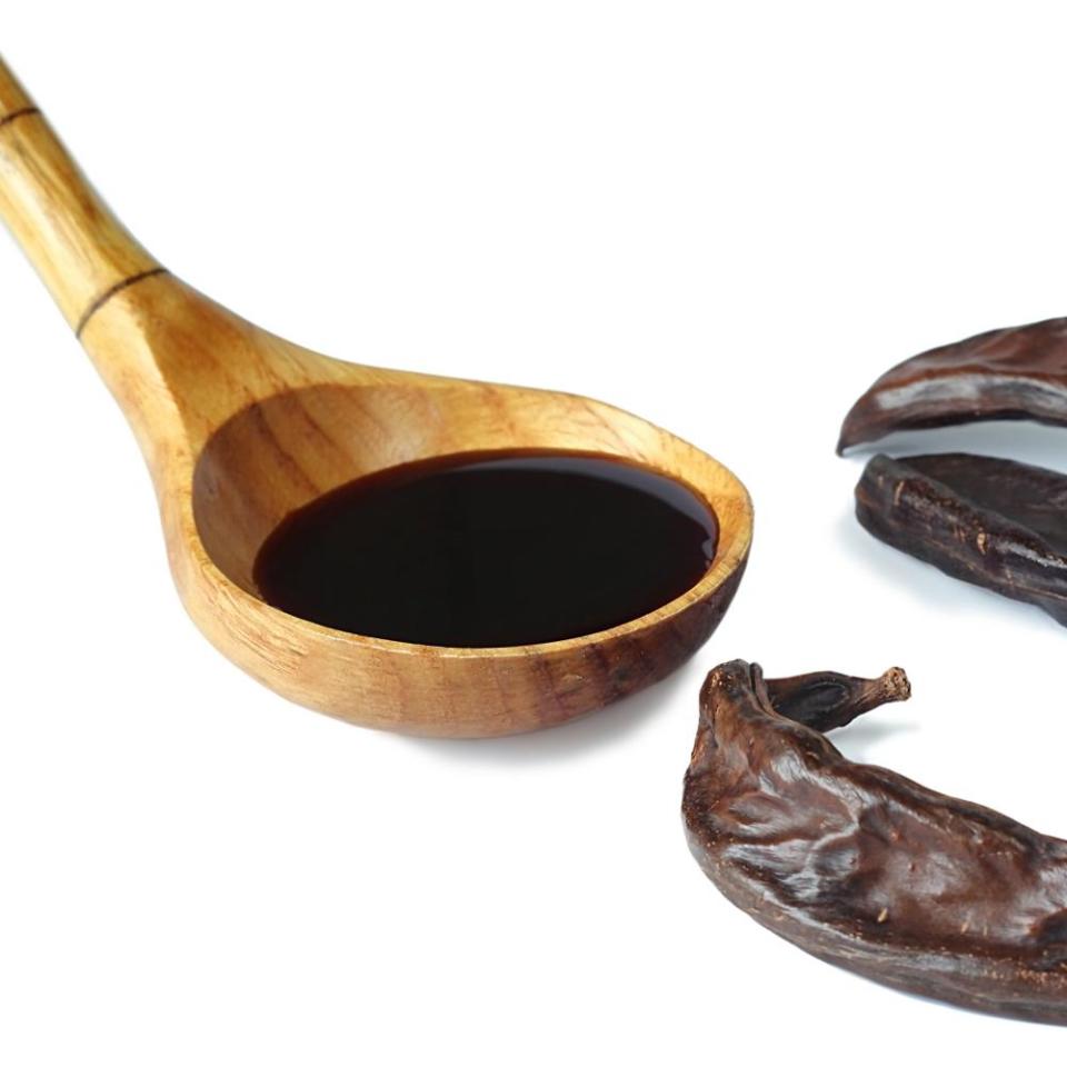 Carob pods and carob syrup in wooden spoon on the white background.