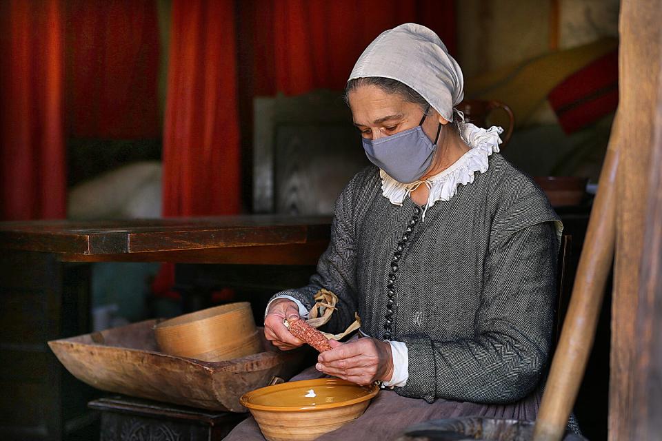 A woman removes corn kernels in her home in Pilgrim Village at Plimoth Patuxet Museums