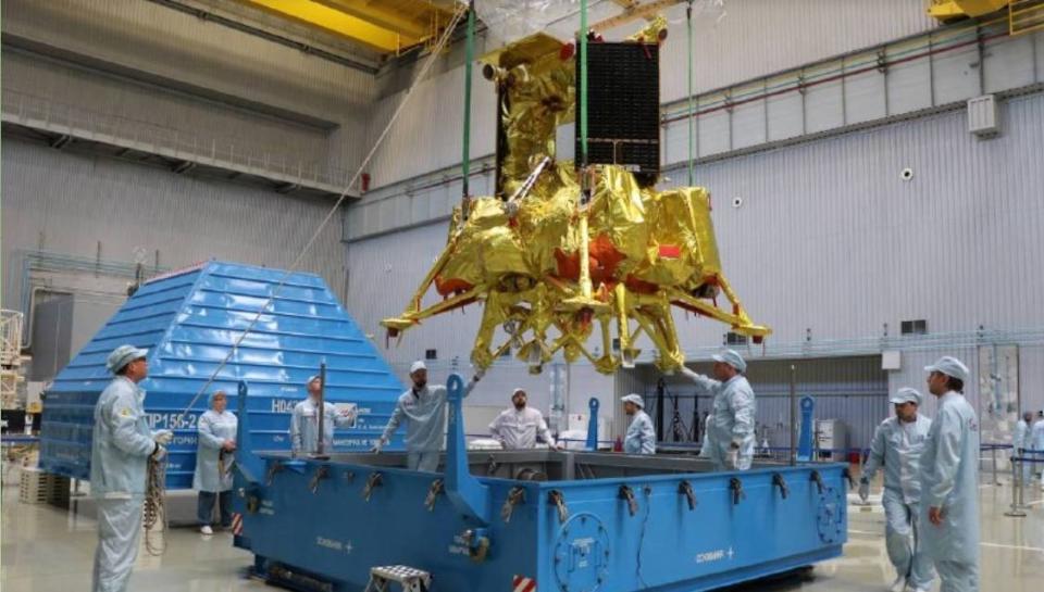 lab technicians in clean suits work on a gold-foil-wrapped spacecraft