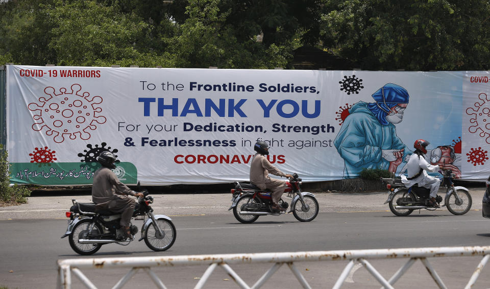 Motorcyclists ride past a banner paying tribute to doctors, nurses, paramedics and other health care providers who are offering care and saving lives during the coronavirus pandemic, hanging along a roadside in Islamabad, Pakistan, Wednesday, July 8, 2020. (AP Photo/Anjum Naveed)