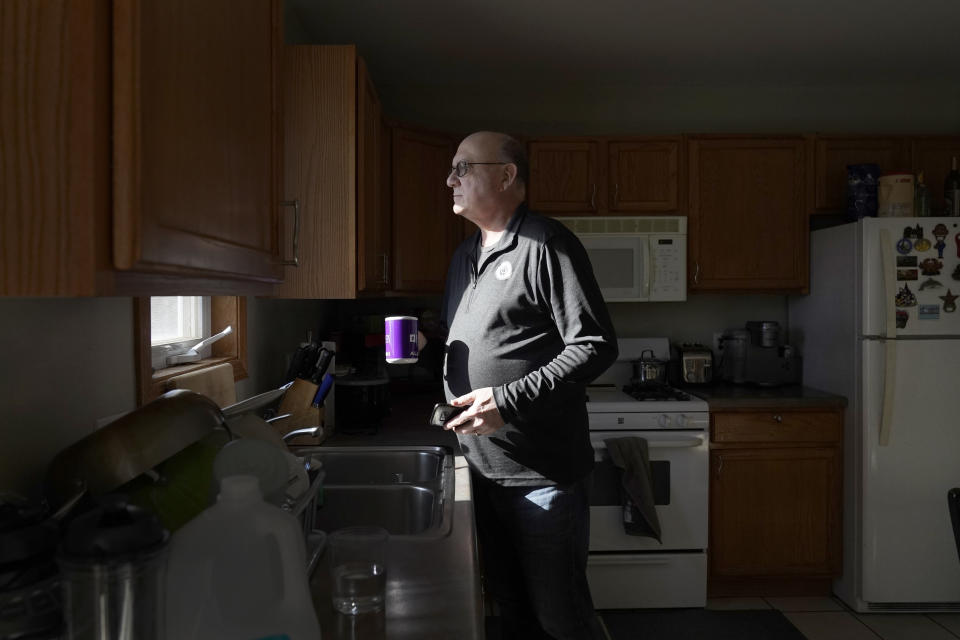 Roger Strukhoff 67, looks out his kitchen window after making a cup pf coffee Thursday, Jan. 20, 2022, in his DeKalb, Ill., home. Strukhoff was being treated for intestinal bleeding at a hospital outside Chicago this month when he suffered a mild heart attack. Normally, the medical staff would have sent Strukhoff to the intensive care unit, but, overrun with COVID-19 patients, the staff instead had to wheel a heart monitor into his room and quickly administer nitroglycerin and morphine. (AP Photo/Charles Rex Arbogast)