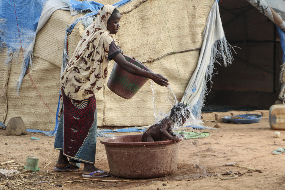 In this Thursday, May 14, 2020, photo, a mother who fled the north after her village was attacked by gunmen, washes her baby outside the tent in Nouna, Burkina Faso, where she now lives and depends on food handouts. Violence linked to Islamic extremists has spread to Burkina Faso's breadbasket region, pushing thousands of people toward hunger and threatening to cut off food aid for millions more. (AP Photo/Sam Mednick)