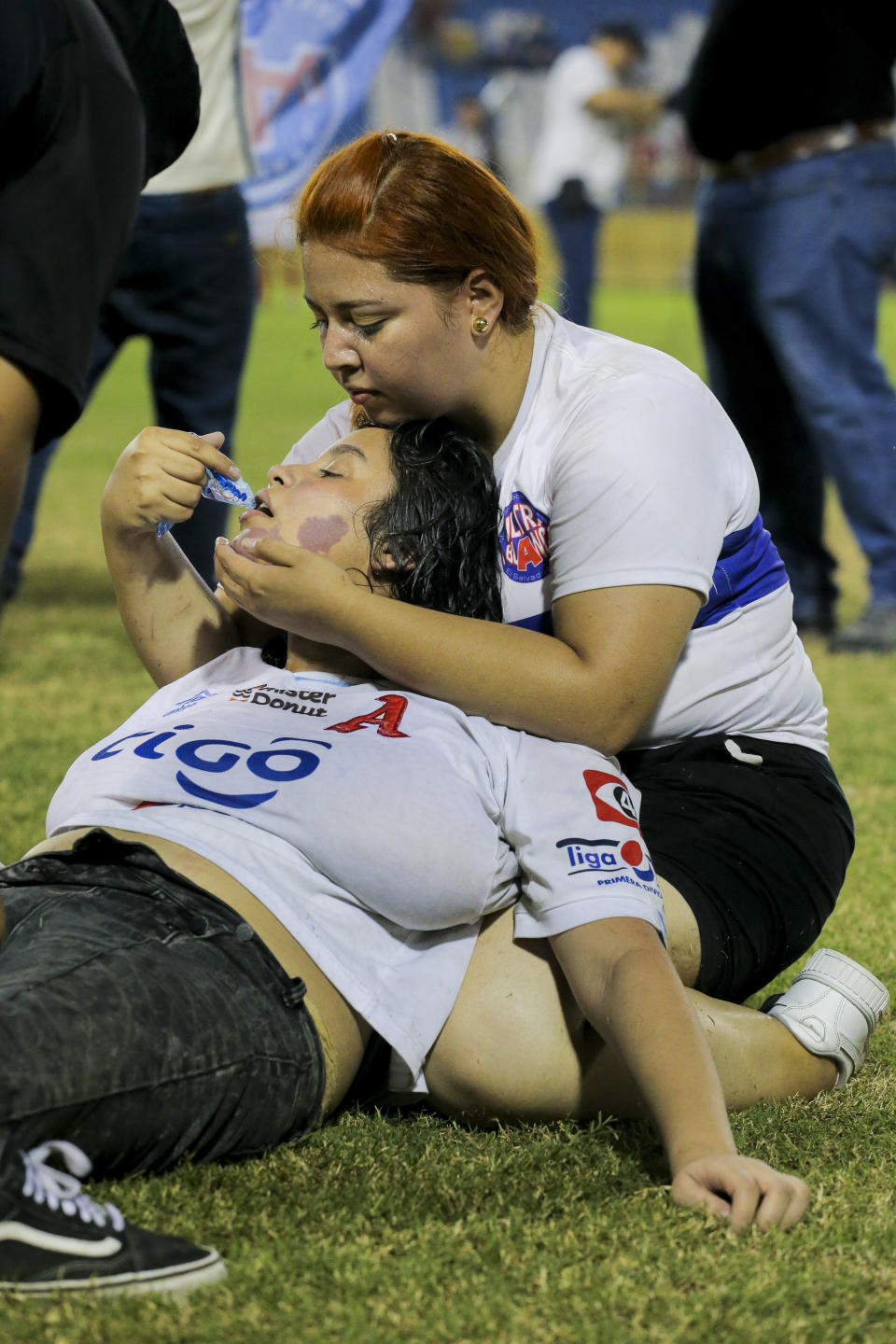 A fan comforts another lying at the field of Cuscatlan stadium in San Salvador, El Salvador, Saturday, May 20, 2023. At least nine people were killed and dozens more injured when stampeding fans pushed through one of the access gates at a quarterfinal Salvadoran league soccer match between Alianza and FAS. (AP Photo/Milton Flores)