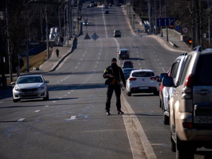 armed police officer stands on a street outside Kyiv with cars going by