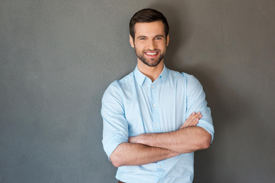 Smiling man in collared shirt with arms crossed against a gray background