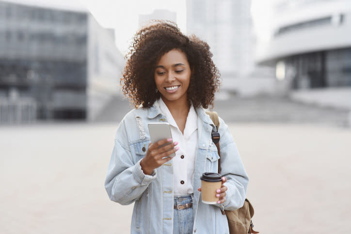 A woman holds a cup of coffee and looks at her phone.