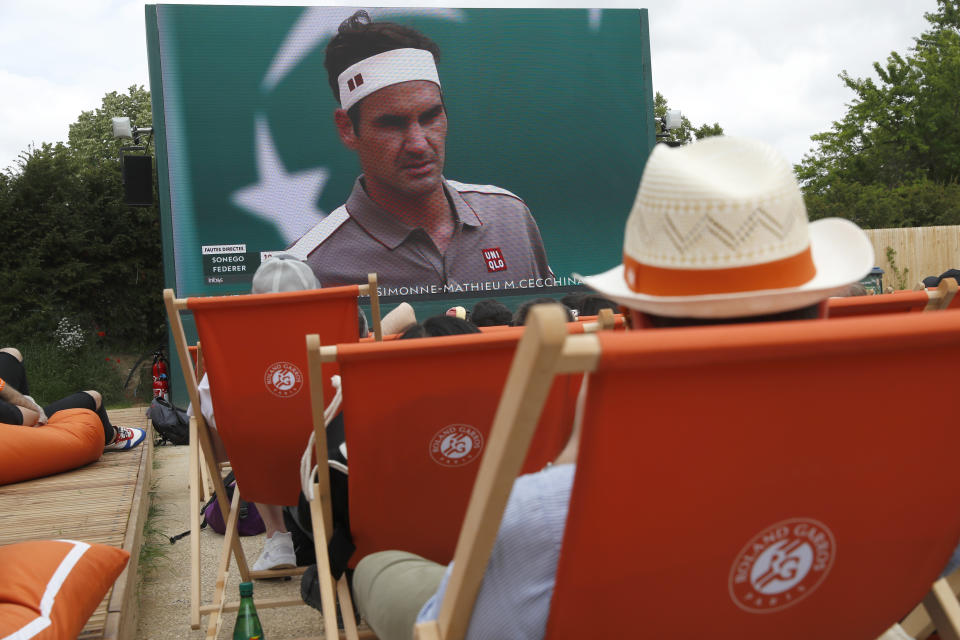 Spectators in lounge chairs watch Roger Federer, on screen, rear, play Italy's Lorenzo Sonego during their first round match of the French Open tennis tournament at the Roland Garros stadium in Paris, Sunday, May 26, 2019. (AP Photo/Pavel Golovkin)