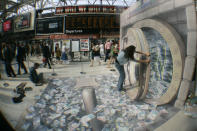 A woman poses in U.S. street artist Kurt Wenner's 3D illustration of an open vault containing British currency, fluttering out at Waterloo station, London, July 24, 2008. (AP Photo/Sang Tan)