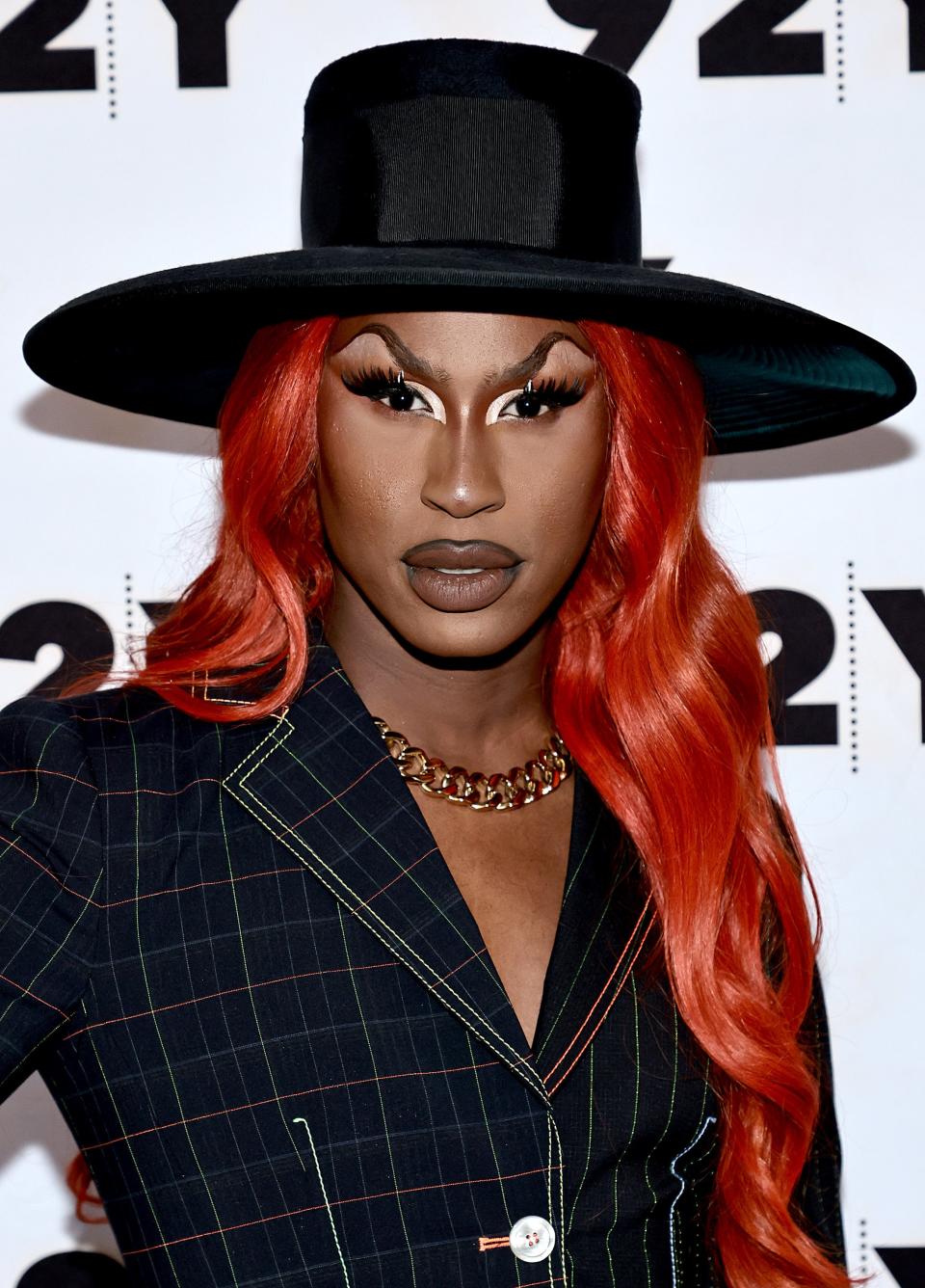 Shea in a pin-striped suit and wide-brimmed hat with red hair at a celebrity event