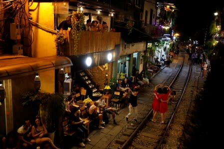 Tourists sit in cafes near a railway track as others take a picture on it, along a street in the Old Quarter of Hanoi, Vietnam