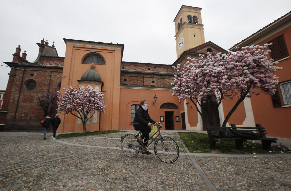 In this photo taken on Thursday, March 12, 2020, a woman wearing a mask rides a bicycle in Codogno, Italy. The northern Italian town that recorded Italy’s first coronavirus infection has offered a virtuous example to fellow Italians, now facing an unprecedented nationwide lockdown, that by staying home, trends can reverse. Infections of the new virus have not stopped in Codogno, which still has registered the most of any of the 10 Lombardy towns Italy’s original red zone, but they have slowed. For most people, the new coronavirus causes only mild or moderate symptoms. For some it can cause more severe illness. (AP Photo/Antonio Calanni)