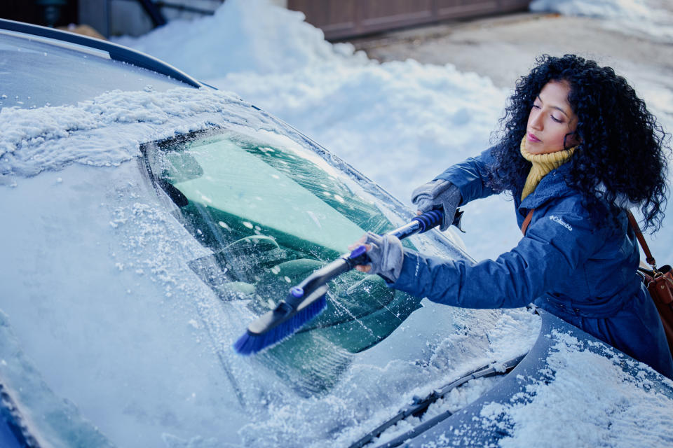 Woman brushing snow off her car&#39;s windshield using a telescoping snowbrush from Canadian Tire