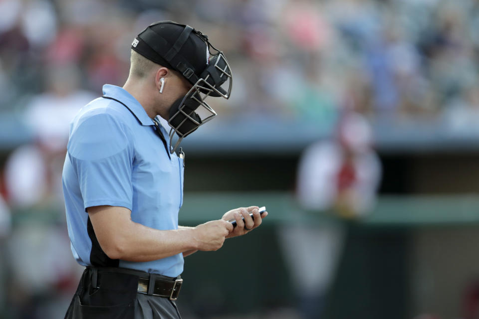 Home plate umpire Brian deBrauwere checks an iPhone while wearing an earpiece prior to the start of the Atlantic League All-Star minor league baseball game, Wednesday, July 10, 2019, in York, Pa. The umpire received information about balls and strikes with the device connected to a TrackMan computer system that uses Doppler radar. The independent Atlantic League became the first American professional baseball league to let the computer call balls and strikes during the all star game. (AP Photo/Julio Cortez)