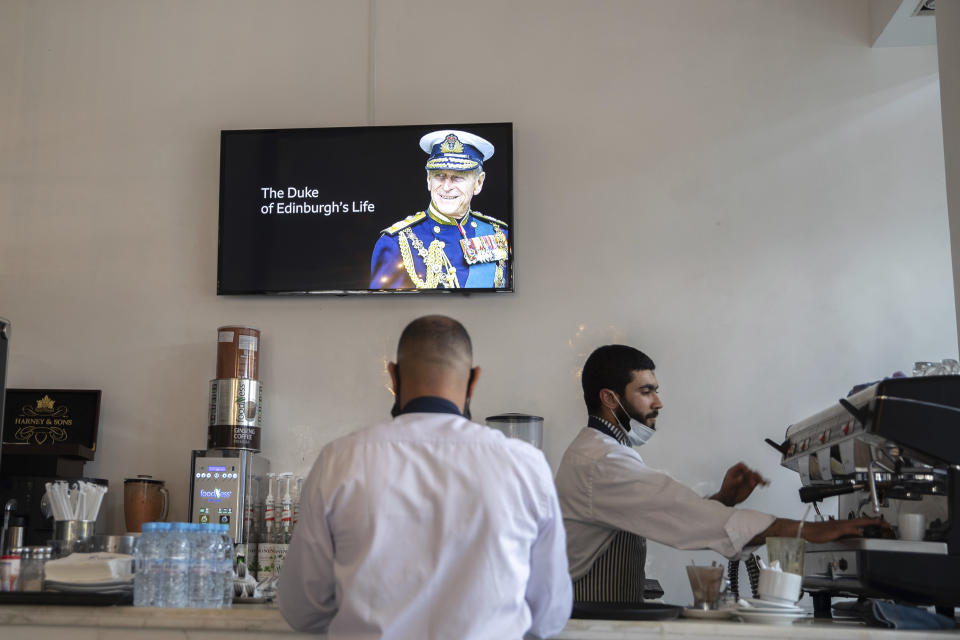 Waiters work at a coffeeshop while a TV shows the news of Prince Philip's death, in Rabat, Morocco, Friday, April 9, 2021. Prince Philip, the irascible and tough-minded husband of Queen Elizabeth II who spent more than seven decades supporting his wife in a role that both defined and constricted his life, has died, Buckingham Palace said Friday. He was 99. (AP Photo/Mosa'ab Elshamy)