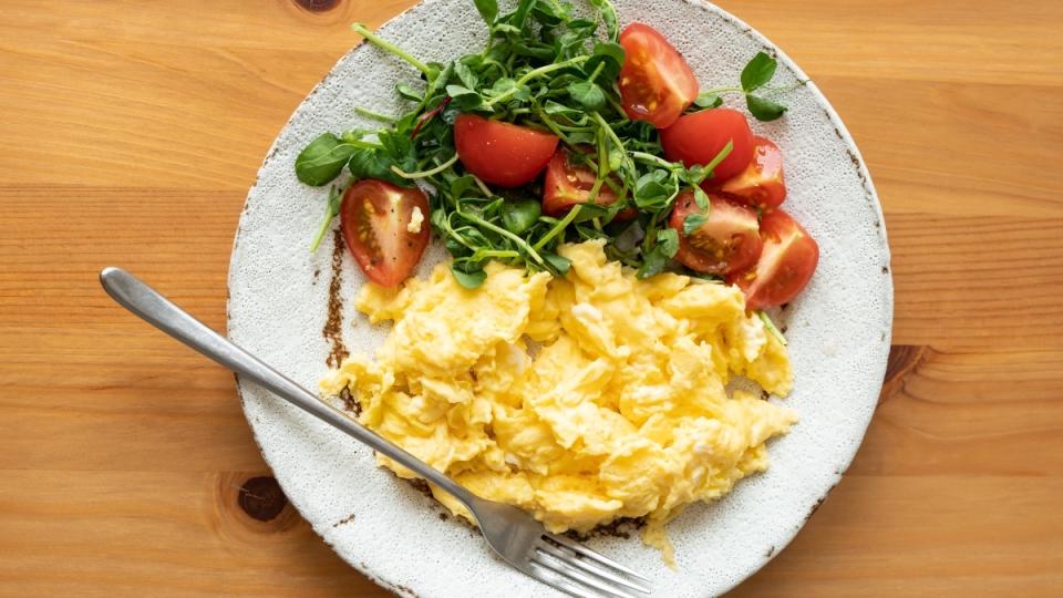 Scrambled eggs on a white plate with tomatoes and arugula, which are food swaps that reduce diabetes risk
