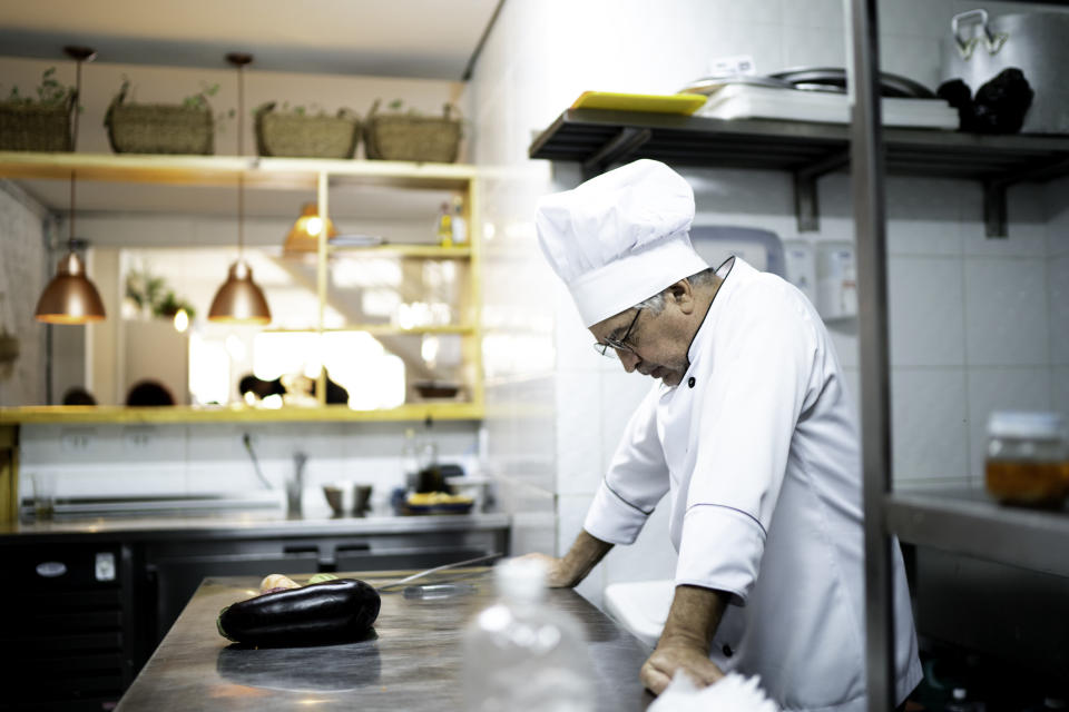 A man wearing a chef's hat in the kitchen looking down