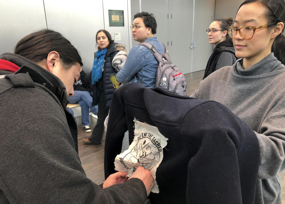 Jeff Chen, left, affixes a "Defend the Sacred" logo to Su Chon's jacket ahead of a Bureau of Land Management hearing Monday, Feb. 11, 2019, in Anchorage, Alaska. The two Anchorage residents planned to oppose drilling as the federal agency accepted public comments on a draft environmental review on drilling within the coastal plain of the Arctic National Wildlife Refuge. (AP Photo/Mark Thiessen)