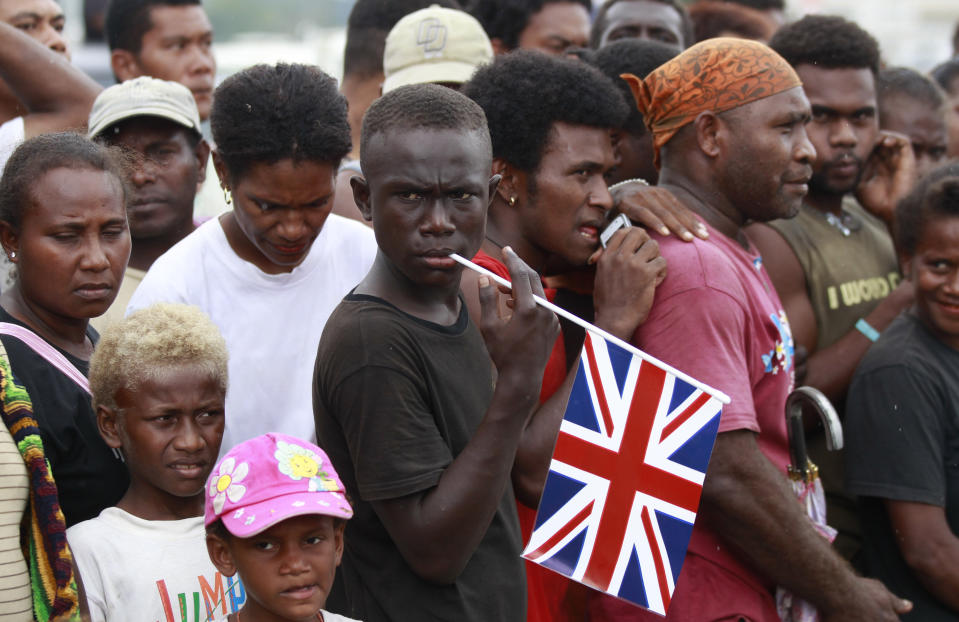 FILE - A well-wisher with a Union flag waits among others before the arrival of Britain's William and his wife Kate, the Duke and Duchess of Cambridge, for the opening ceremony of the renovated Commonwealth Street in central Honiara, Solomon Islands, Monday, Sept. 17, 2012. After seven decades on the throne, Queen Elizabeth II is widely viewed in the U.K. as a rock in turbulent times. But in Britain’s former colonies, many see her as an anchor to an imperial past whose damage still lingers. (Daniel Munoz, Pool Photo via AP, File)