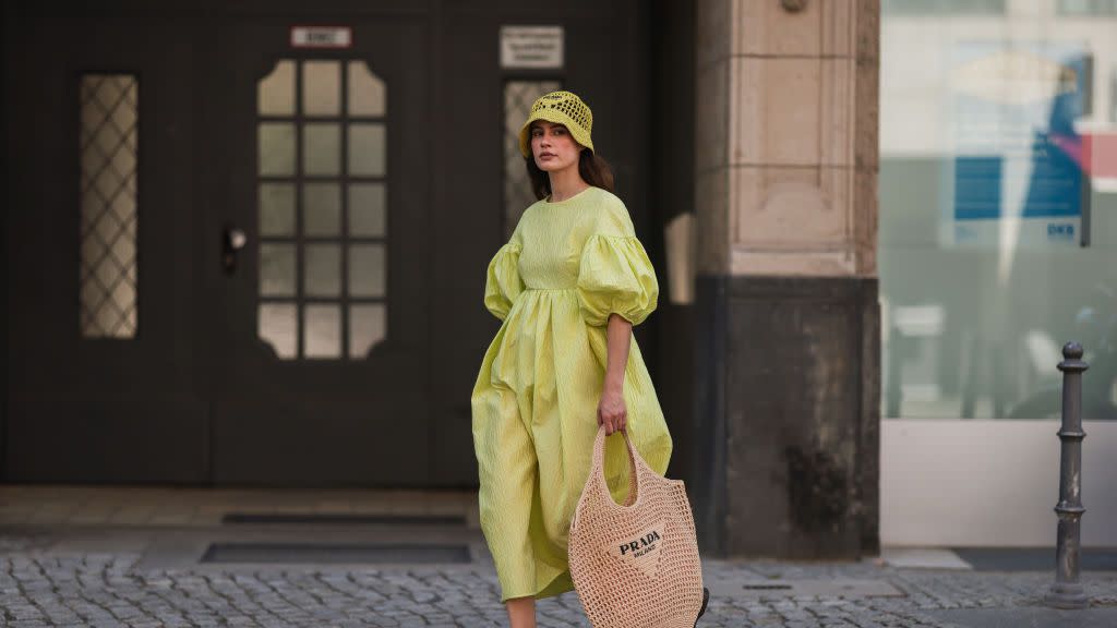 a woman carrying a prada crochet tote bag with a yellow dress and clogs on the street in berlin in a roundup of the best crochet tote bags