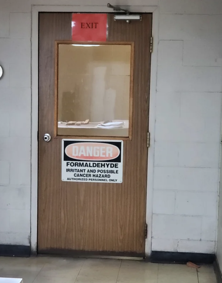 A sign on the top of the door says "exit," but a sign on the bottom of the same door says "Danger: Formaldehyde, irritant and possible cancer hazard"