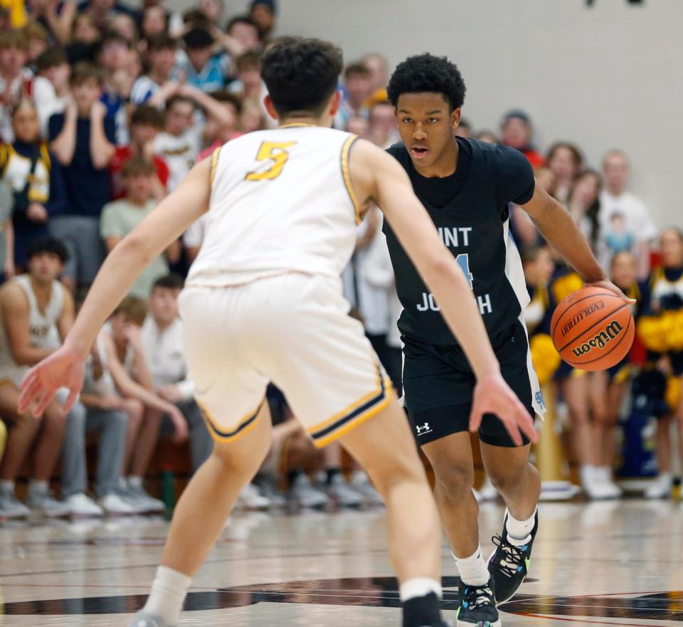 South Bend Saint Joseph freshman Elijah King, background, looks to dribble around a Delta defender during the IHSAA Class 3A boys basketball semistate championship game Saturday, March 16, 2024, at Logansport High School.