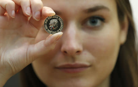 A gallery assistant poses with a 2-pound coin with the new portrait of Britain's Queen Elizabeth following it's unveiling at the National Portrait Gallery in London, March 2, 2015. REUTERS/Suzanne Plunkett