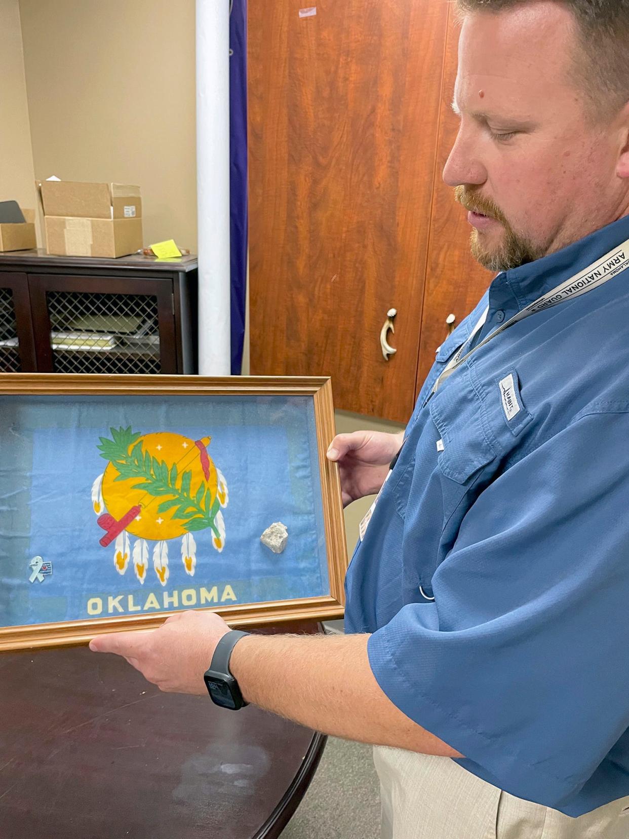Kyle Genzer, principal of Mannford High School in Mannford, keeps a framed flag and fragment from the Alfred P. Murrah Federal Building on the wall in front of his desk in his office. He is the son of Jamie Genzer, who was 32 when she died in the 1995 bombing of the federal building in Oklahoma City. [Photo by Pam Olson]