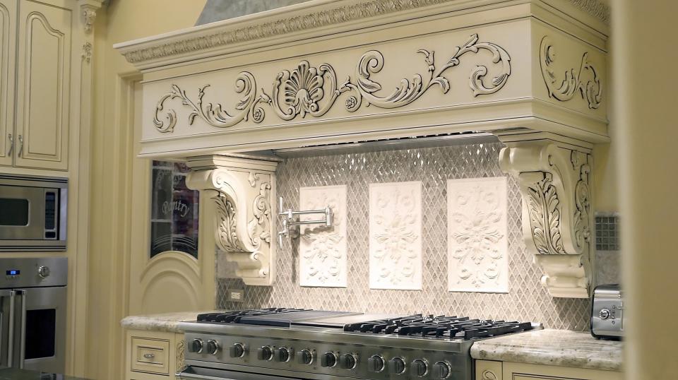 A stove so large, it has 12 knobs for different burners, and it is adorned with an ornate overhang and backsplash