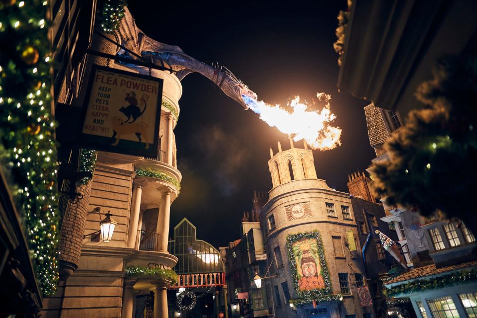 Festive decorations and dragon fire illuminate Diagon Alley in the Wizarding World of Harry Potter.