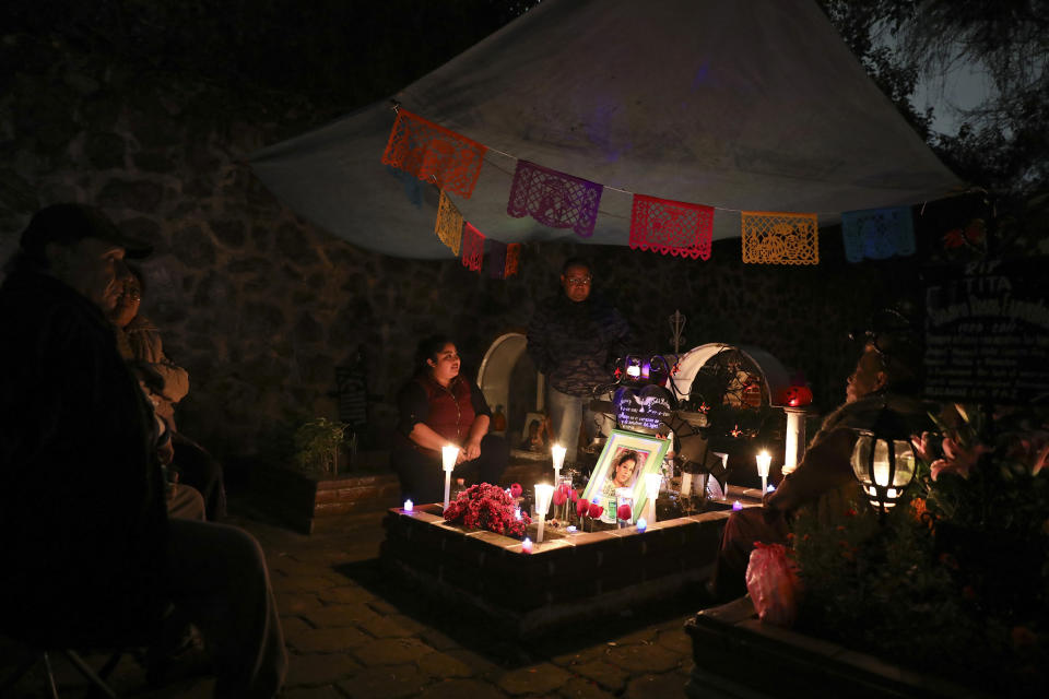 Relatives spend the night next to the tomb of their loved one in the Los Reyes cemetery during Day of the Dead festivities in Mexico City, Friday, Nov. 1, 2019. In a tradition that coincides with All Saints Day and All Souls Day, families decorate the graves of departed relatives with flowers and candles, and spend the night in the cemetery, eating and drinking as they keep company with their deceased loved ones. (AP Photo/Eduardo Verdugo)