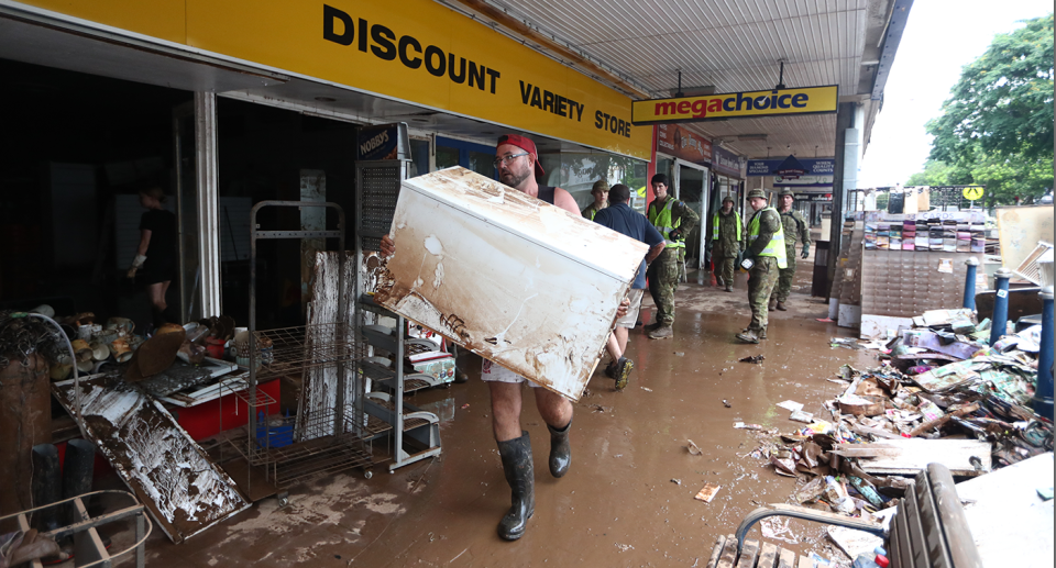 A male cleanup volunteer carries whitegoods out of a shop damaged by flooding.