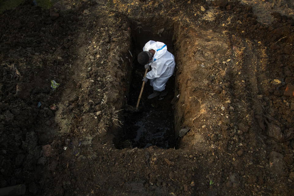 A man in protective suit digs earth to bury the body of a person who died of COVID-19 in Gauhati, India, Sunday, April 25, 2021. Delhi has been cremating so many bodies of coronavirus victims that authorities are getting requests to start cutting down trees in city parks, as a second record surge has brought India's tattered healthcare system to its knees. (AP Photo/Anupam Nath)