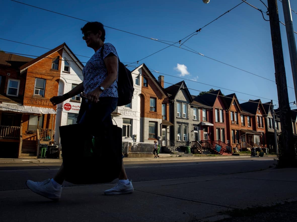 A person walks by a row of houses in Toronto in this photo taken last July. If approved and put into action, Tory's 'housing action plan' would see the city's housing makeup change significantly in the coming years. (Cole Burston/Canadian Press - image credit)