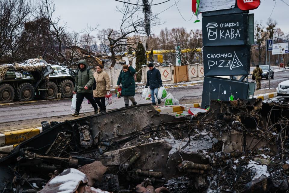 Residents carrying supplies walk on a road amid destruction.