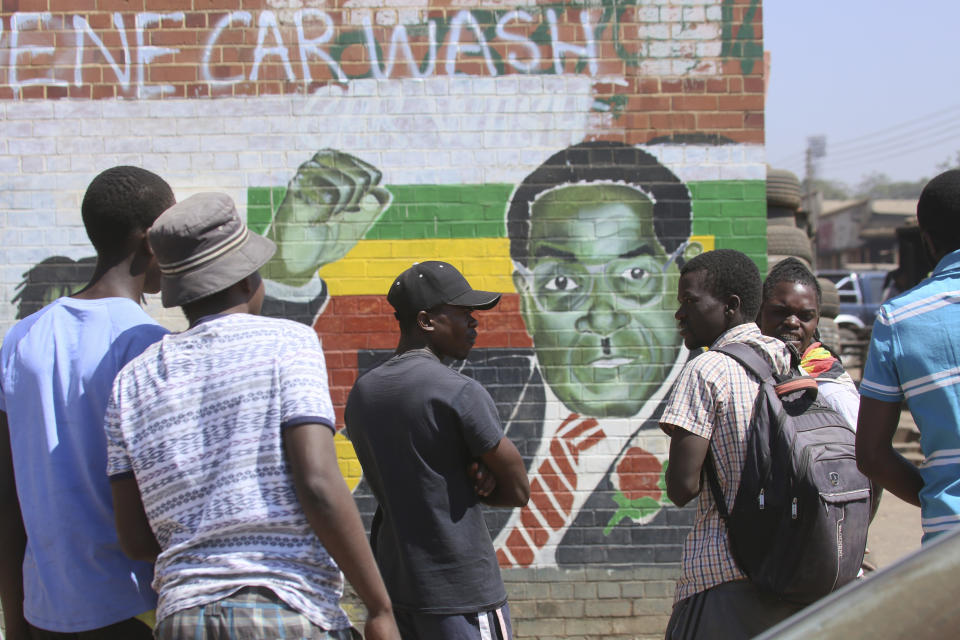 People gather around a portrait of former Zimbabwean President Robert Mugabe in Harare, Friday, Sept. 6, 2019. Robert Mugabe, the former leader of Zimbabwe forced to resign in 2017 after a 37-year rule whose early promise was eroded by economic turmoil, disputed elections and human rights violations, has died. He was 95. (AP Photo/Tsvangirayi Mukwazhi)