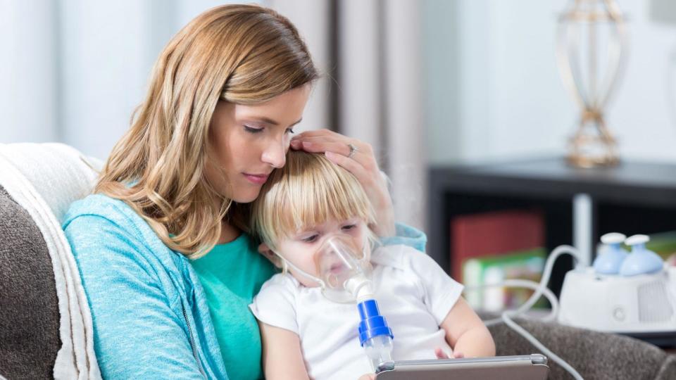 A woman holds a child with an oxygen mask on