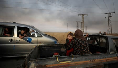 FILE PHOTO: A woman with a baby sits at a back of a truck as they flee Ras al Ain town