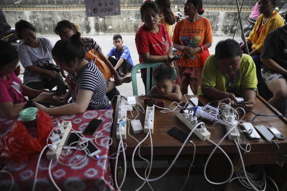 People check their phones at a charging station for those affected by floods in Jakarta, Indonesia, Saturday, Jan. 4, 2020. Monsoon rains and rising rivers submerged parts of greater Jakarta and caused landslides in Bogor and Depok districts on the city's outskirts as well as in neighboring Lebak, which buried a number of people. (AP Photo/Dita Alangkara)