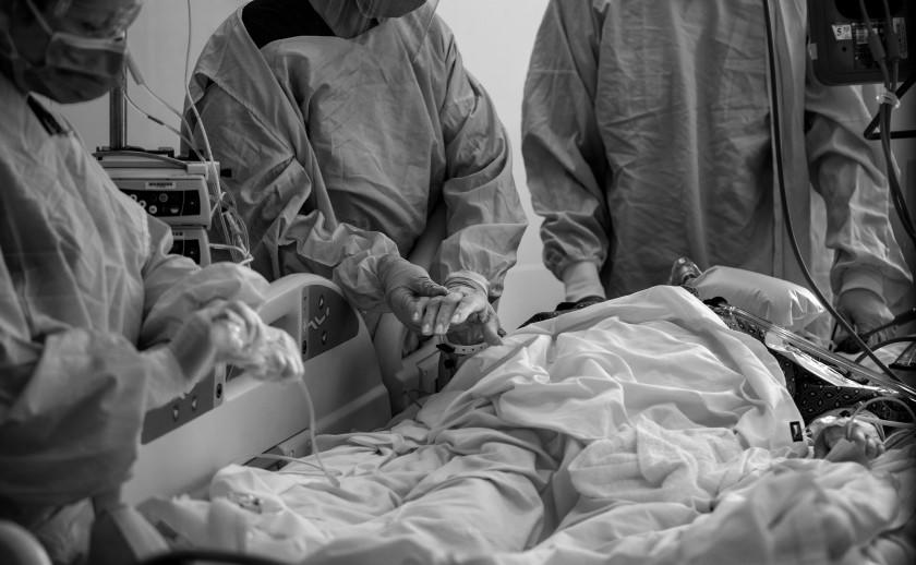 LOMA LINDA, CA - DECEMBER 15, 2020: A nurse holds a COVID-19 patient's hand before she is intubated by a medical team led by pulmonologist Dr. Laren Tan, right, in the ICU at Loma Linda University Medical Center on December 15, 2020 in Loma Linda, California. The hospital is experiencing a huge surge in COVID-19 patients. Dr. Michael Matus, chief of hospitalist said they are currently admitting more than 15 patients a day. The hospital has added 5 additional Covid units in addition to ICU. Many of the ICU patients have underlying health issues. Once those patients get Covid, "It's a marathon that they can't run, said Dr. Tan.