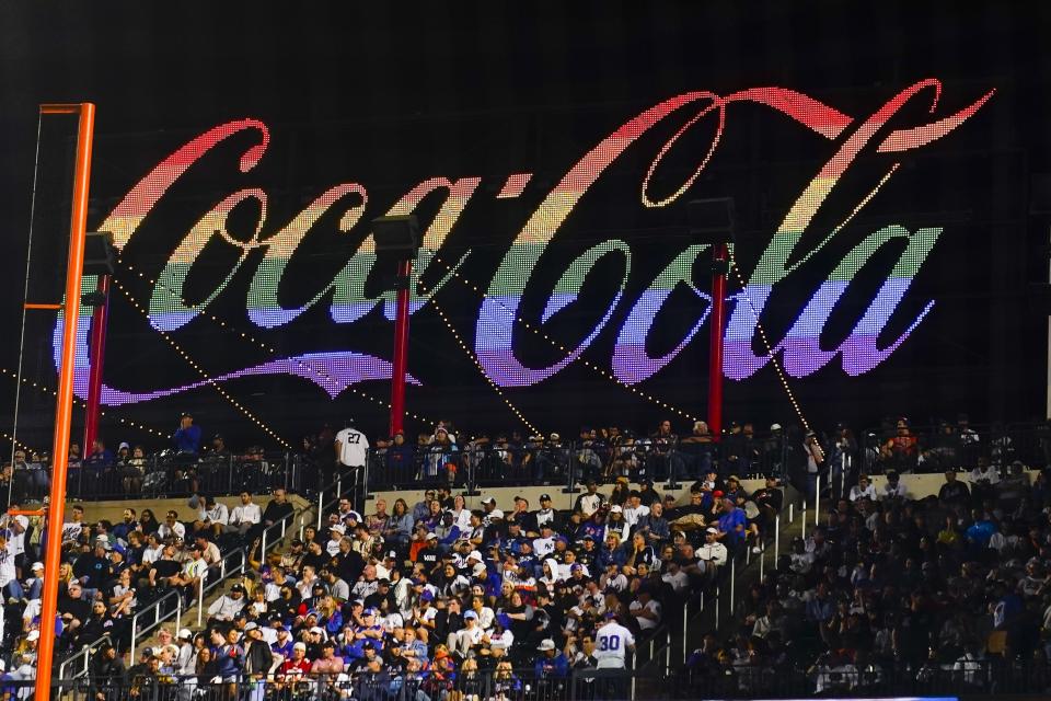 Fans sit in front of a rainbow-colored Coca-Cola sign during the seventh inning of a baseball game between the New York Mets and the New York Yankees on Wednesday, June 14, 2023, in New York. (AP Photo/Frank Franklin II)