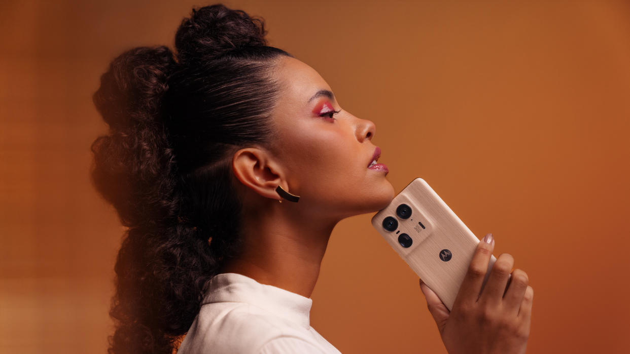  A person holding the Motorola Edge 50 Ultra on an orange background. 