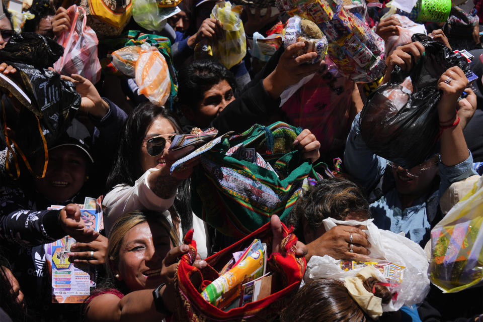 Personas llevan casas en miniatura y billetes falsos a bendecir por un cura católico a las afueras de la iglesia de San Francisco durante la feria anual de Alasita en La Paz, Bolivia, el miércoles 24 de enero de 2024. En el día de inauguración de la feria se ofrecen réplicas en miniatura de las cosas que las personas anhelan o desean, como casas, vehículos o salud, para que se conviertan en realidad. Alasita es una palabra aymara que significa "cómprame". (AP Foto/Juan Karita)