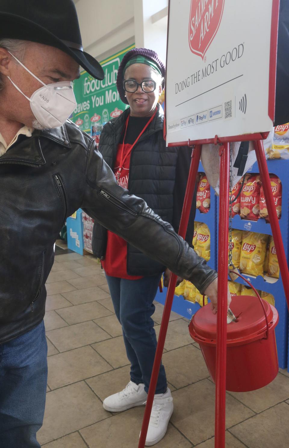 Dane Stotzer stuffs the red kettle as Salvation Army volunteer Diane Hill rings her bell Tuesday at the Acme Fresh Market in Montrose .