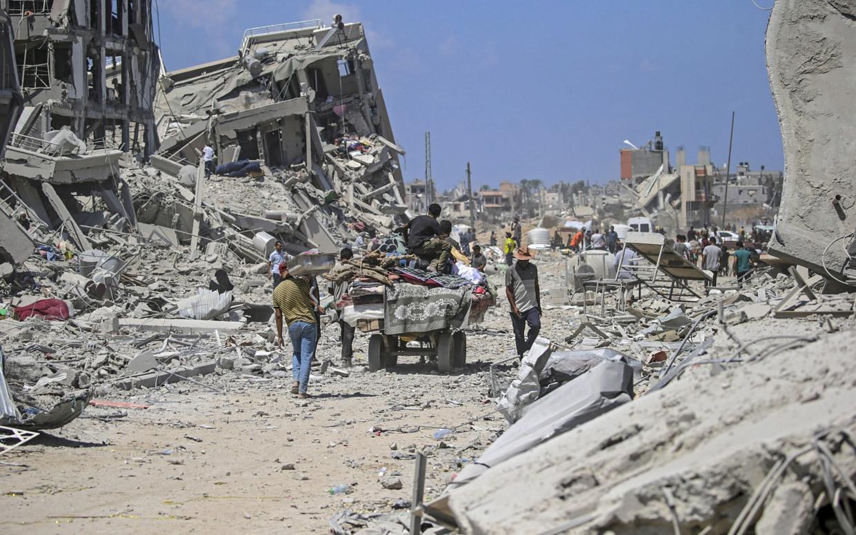 Internally displaced Palestinians walk past their destroyed houses as they return to Deir Al Balah town after the Israeli military pulled out troops