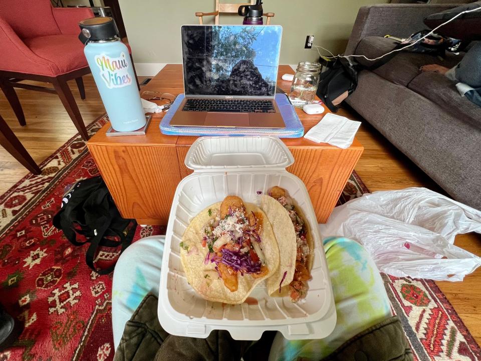 tacos on lap in takeout container, laptop in the background